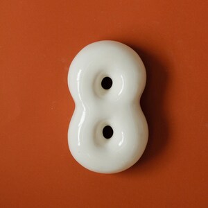 May include: White ceramic number eight with two holes. The number is on a solid orange background.
