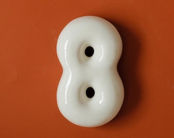 May include: White ceramic number eight with two holes. The number is on a solid orange background.