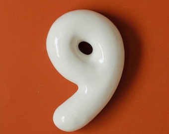 May include: White ceramic number nine with a hole in the center, against a solid orange background.