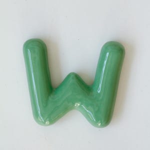 May include: A green ceramic letter W. The letter is in a bubbly, rounded font.