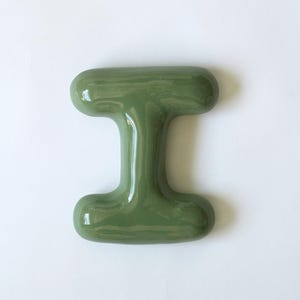 May include: A green ceramic letter I. The letter is made of a smooth, glossy material and has a rounded shape.