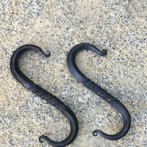 May include: Two black metal hooks with a twisted design. The hooks have a decorative curl at the top.