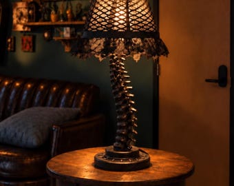 May include: A table lamp featuring a base shaped like a human spinal column in a dark finish. The lamp has a conical shade with a black lattice pattern and a decorative black lace trim along the bottom edge, emitting a warm light.