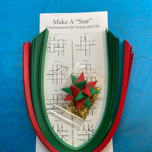 May include: A craft kit for making a paper star. The kit includes green and red paper strips, gold glitter, and instructions with diagrams. The instructions include the text "Make A "Star" Entertainment for Young and Old".