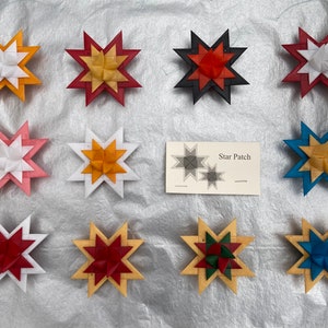 May include: A collection of colorful star-shaped ornaments. The stars feature various color combinations, including red, white, yellow, pink, and blue. A small card with the text "Star Patch" is also present. These ornaments are likely for holiday or craft projects.