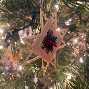May include: A wooden star ornament with a red and green star in the center, hanging on a Christmas tree.