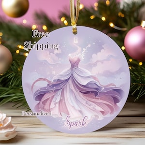 May include: Round ornament with a watercolor illustration of a flowing gown in shades of purple and pink. The word "Spark" is written in a script font at the bottom. A gold ribbon is attached for hanging.