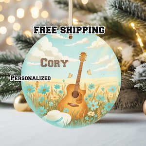 May include: A round, personalized ornament featuring a guitar, flowers, and a hat. The ornament has the name "Cory" and the words "Personalized" and "Free Shipping". The background depicts a field with blue flowers and butterflies.
