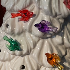 May include: A white ceramic Christmas tree with colorful bird ornaments. The birds are red, purple, green, and orange.