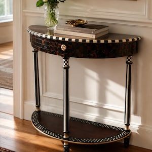 May include: A half-moon console table with a dark brown mosaic top and a black and white checkered border. The table has black legs with gold accents and a lower shelf. A vase of white roses and books sit on top.