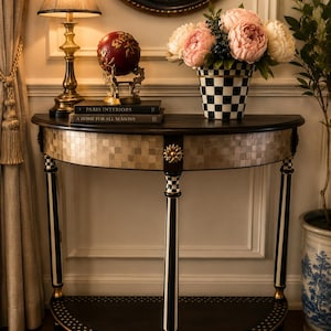 May include: A half-moon console table with a black and gold mosaic top, black and white striped legs, and a lower shelf. A lamp, a decorative globe, and a vase of flowers sit on the table. The table is a decorative piece of furniture.