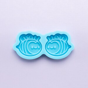 May include: A light blue silicone mould with two bee-shaped cavities. Each bee has a smiling face and a pair of wings.