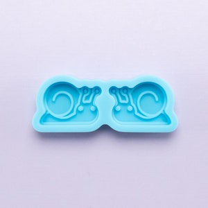May include: A light blue silicone mold with two snail shapes. The mold is designed to create small snail-shaped decorations.