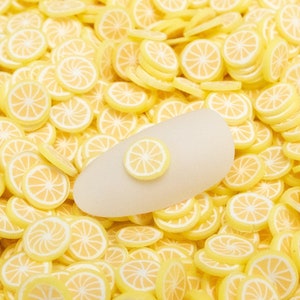 May include: A close-up image of a large quantity of yellow lemon slice shaped embellishments. The embellishments are made of polymer clay and are perfect for adding a touch of summer to crafts.