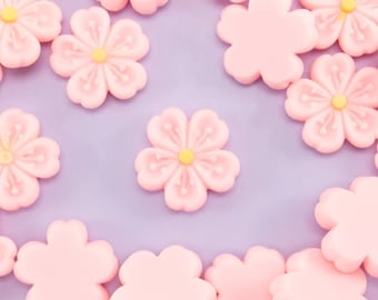 May include: A collection of pink flower-shaped candy decorations on a light purple background. The candy is arranged in a random pattern.