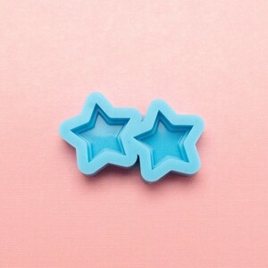 May include: Two blue silicone star-shaped molds on a pink background.
