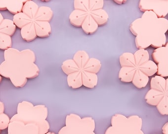May include: A close-up of a light purple surface covered with pink, five-petal flower shapes. The flower shapes are arranged in a circular pattern with a gap in the center.