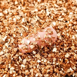 May include: A close-up of a pink fingernail covered in gold glitter flakes.