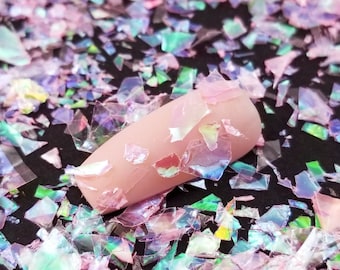 May include: Pink iridescent glitter flakes on a black background. The glitter is in various shapes and sizes.