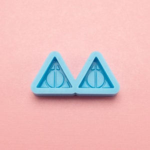 May include: Two light blue silicone molds shaped like triangles with a circle inside each triangle. The circle has a symbol inside it that resembles a lightning bolt.