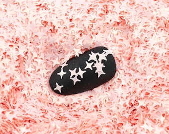 May include: A black oval-shaped nail with white star-shaped designs on a pink background of confetti stars.