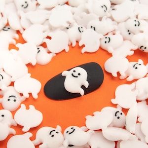 May include: A black nail with a white ghost design surrounded by many white ghost charms on an orange background.