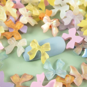 May include: Assortment of pastel colored plastic bows in various shapes and sizes. The bows are scattered on a light green surface.