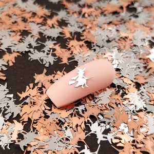 May include: A close-up of a nail with a silver witch silhouette on a bed of silver and copper witch silhouettes.
