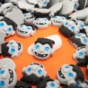 Peut inclure: Une collection de petites figurines en céramique blanche et grise avec des cheveux noirs et des yeux bleus. Les figurines ont une apparence de monstre de dessin animé avec des crocs et un sourire malicieux.