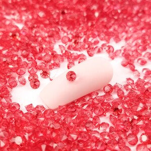 May include: A single, light pink pill or capsule resting on a bed of small, bright red, faceted rhinestones.