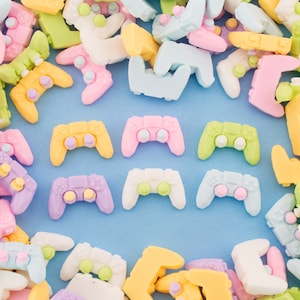 May include: A collection of pastel-colored plastic game controllers in various shapes and sizes. The controllers are arranged in a circle on a light blue background.