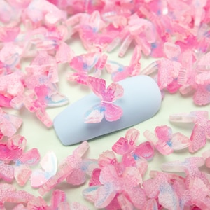 May include: A light blue nail with a pink and blue butterfly nail charm. The nail is surrounded by many pink and blue butterfly charms.