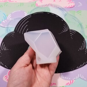 May include: A clear silicone mold shaped like a diamond. The mold is being held in a hand.