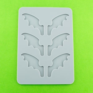 May include: Gray silicone mold with four bat wing shapes. The mold is designed for making small, decorative items.