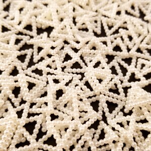 May include: A close-up of a white pearl bead garland, arranged in a repeating star pattern. The beads are small and uniform in size, creating a delicate and elegant look.