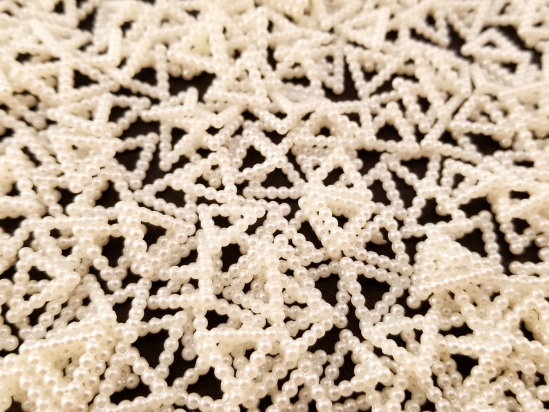 May include: A close-up of a white pearl bead garland, arranged in a repeating star pattern. The beads are small and uniform in size, creating a delicate and elegant look.