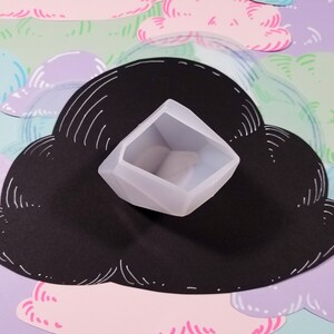 May include: A light gray, geometric-shaped silicone mold for resin casting. The mold is sitting on a black cloud-shaped background.