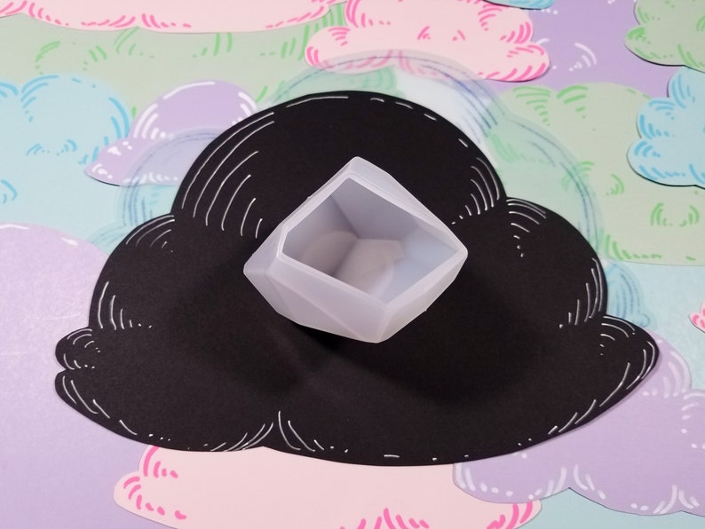 May include: A light gray, geometric-shaped silicone mold for resin casting. The mold is sitting on a black cloud-shaped background.