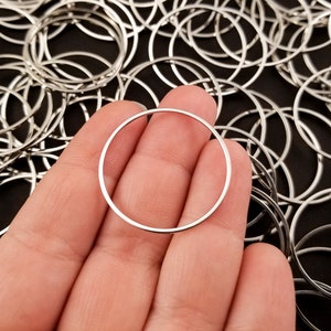 May include: A silver jump ring, approximately 1 inch in diameter, held in a hand against a background of many similar rings.