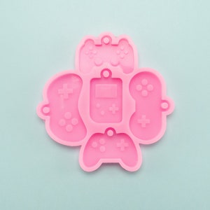 May include: Pink silicone mould with five different shapes of video game controllers and a handheld games console.