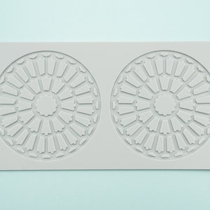 May include: A gray silicone mold with two circular designs. Each design features a circular pattern with a smaller circle in the center.