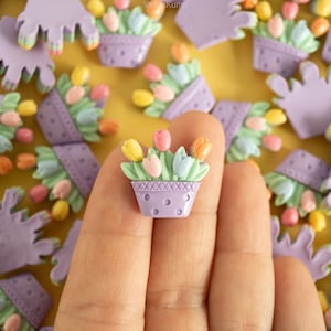May include: A close-up of a purple flower pot with a white polka dot pattern and a cluster of pastel pink, yellow, and blue tulips. The pot is surrounded by other flower pots with similar designs.