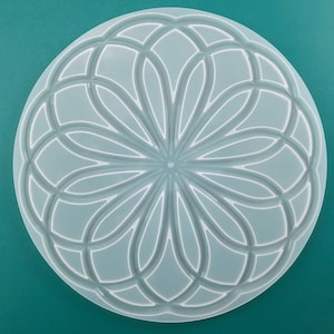 May include: A white circular silicone mold with a detailed geometric design. The design features a repeating pattern of curved lines that create a flower-like shape in the center.