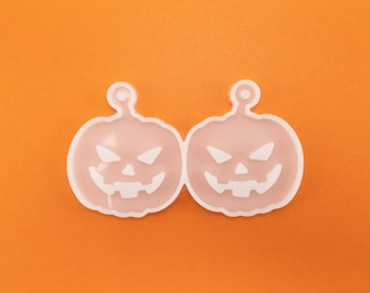 May include: Two white plastic pumpkin-shaped molds with jack-o'-lantern faces. The molds are on a bright orange background.