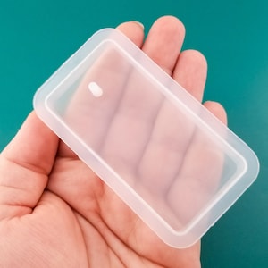 May include: A clear, rectangular silicone mold with a raised edge. The mold is designed for making small, rectangular objects.
