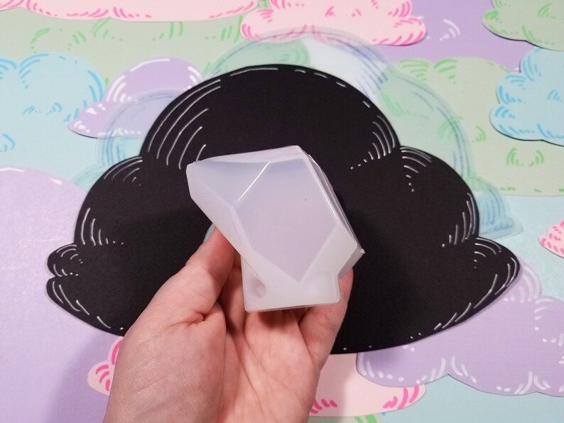 May include: A clear silicone mold shaped like a diamond. The mold is being held in a hand.