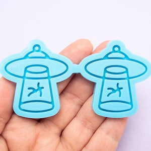 May include: Two light blue silicone molds shaped like flying saucers with an alien inside. The molds are for making resin crafts.
