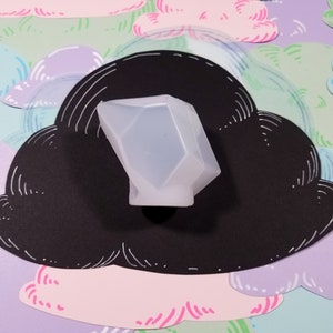 May include: A clear, translucent, geometrically shaped silicone mold for making resin crafts. The mold is sitting on a black cloud-shaped background with a white outline.