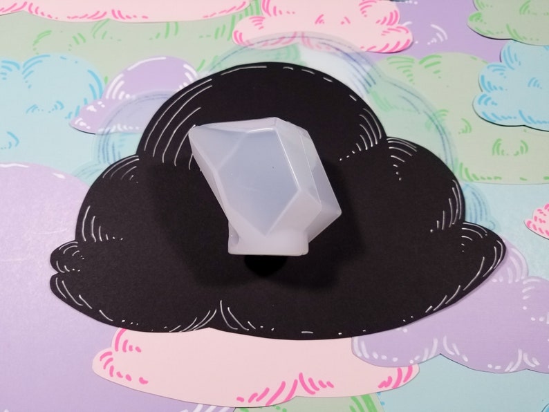 May include: A clear, translucent, geometrically shaped silicone mold for making resin crafts. The mold is sitting on a black cloud-shaped background with a white outline.