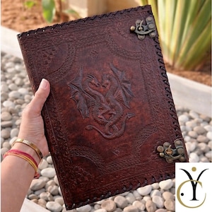 May include: A dark brown leather journal with a detailed embossed dragon design on the cover. The journal features decorative stitching along the edges and a metal clasp closure. The cover is a rich, reddish-brown color.